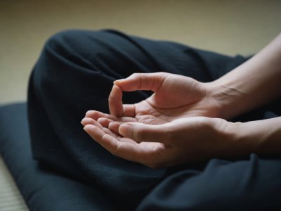 Κοντινό πλάνο χεριών που σχηματίζουν μούδρα σε σχήμα ωοειδούς, να αναπαύονται στην αγκαλιά πάνω σε σκούρο ύφασμα